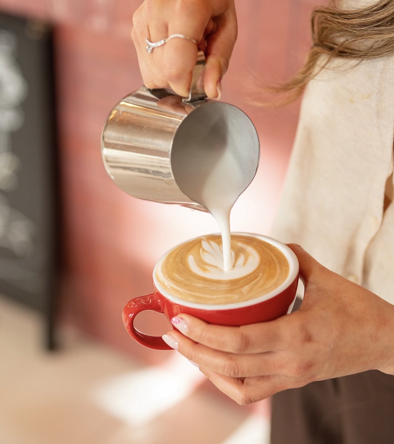 Latte art en cours de préparation, lait versé dans une tasse rouge